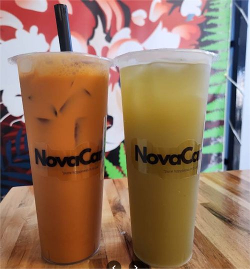 A cup of Thai tea beside a cup of sugarcane juice in front of the mural.